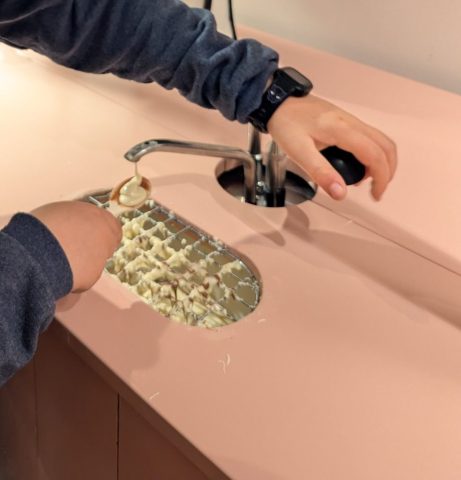 experienta-interactiva-de-turnare-a-ciocolatei-albe-in-muzeul-ciocolatei-din-zagreb Copil folosind o pompă de ciocolată albă pentru a turna compoziția pe un grilaj în cadrul unei activități interactive