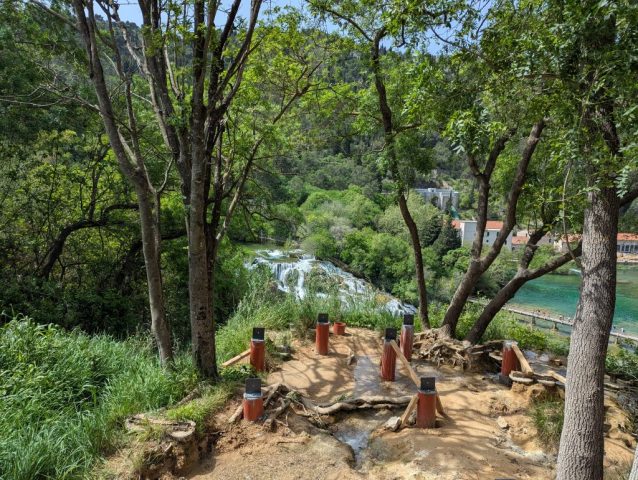 privire-catre-skradinski-buk-parc-national-krka-croatia Privire de sus către cascada Skradinski Buk din Parcul Național Krka, Croația, printr-o deschidere între copaci.